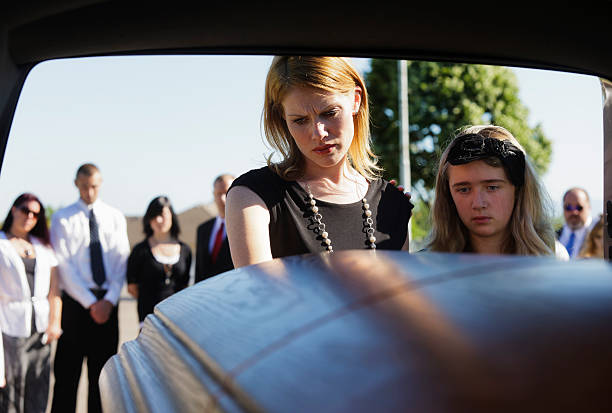 Grieving Widow A grieving woman standing at the rear of a hearse looking down at the casket. Taken from within the hearse. child casket stock pictures, royalty-free photos & images