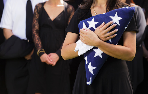 A woman holding a folded American flag at a funeral.