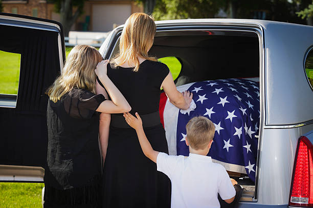 Grieving Family at a Funeral A woman and two children standing behind an open hearse. hearse photos stock pictures, royalty-free photos & images