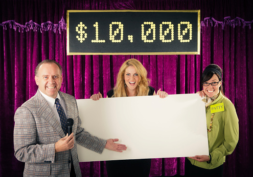 An old fashioned game show host holding a microphone standing with the contestant and assistant. Photographed in studio with a purpose built set and props.