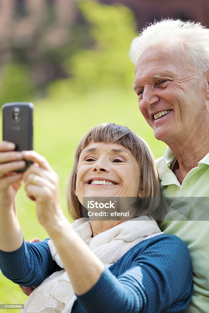 Mature Couple Taking Pictures With Smartphone Cheerful mature couple taking pictures outdoors with a modern smartphone. Active Seniors Stock Photo