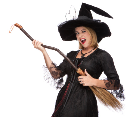 Extremely happy positive overjoyed young woman wizard wearing witch costume holding in hand broom isolated over beige background screaming with excitement clenched fists
