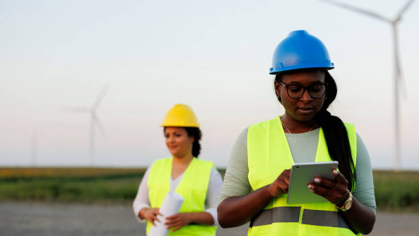 istock Two Female Engineer wearing uniform ,helmet hold document inspection work in wind turbine farms rotation to generate electricity energy. 1732006925