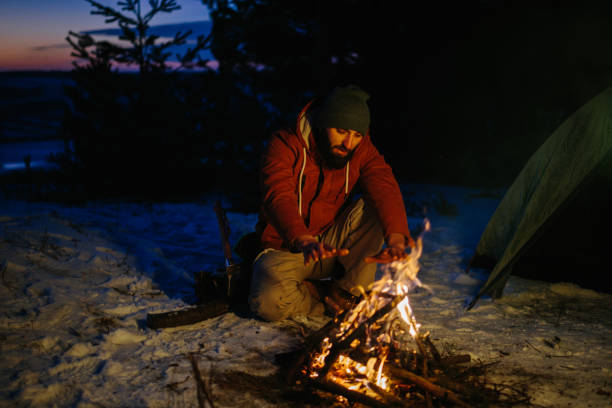 istock A man sits near a campfire, warming himself by the fire in a winter forest at sunset. 1732016779