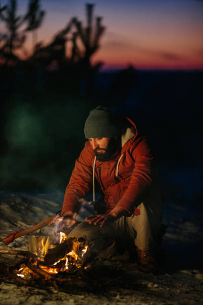 istock A man sits near a campfire, warming himself by the fire in a winter forest at sunset. 1732016919