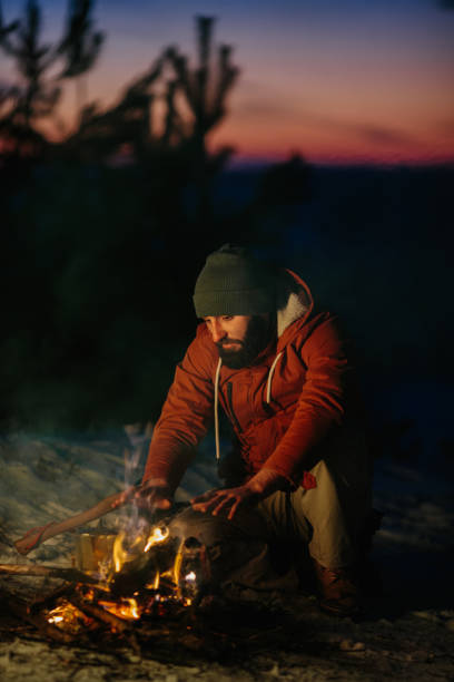 istock A man sits near a campfire, warming himself by the fire in a winter forest at sunset. 1732016925
