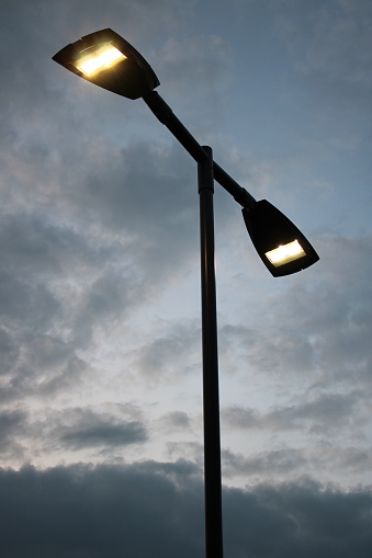 Modern Street light with two lights attached illuminated, cloudy sky in background