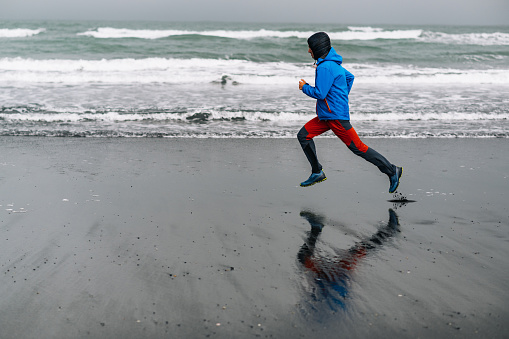 A fit runner is exercising in the wild nature on the ocean shore in Iceland. A sportsman in shape is practicing during the gale in extreme weather.