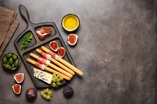 Bread sticks grissini with prosciutto, blue cheese, figs and olives on table, closeup. Italian antipasti . Top view, flat lay, copy space