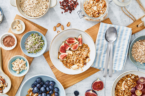 Healthy granola muesli oatmeal for breakfast, preparation with fresh organic fruit, nuts and grains, at a white granite table in a modern white kitchen, representing a wellbeing and a healthy lifestyle, city life, fast life, healthy habits and smart eating, nutrient rich food, an image with a copy space