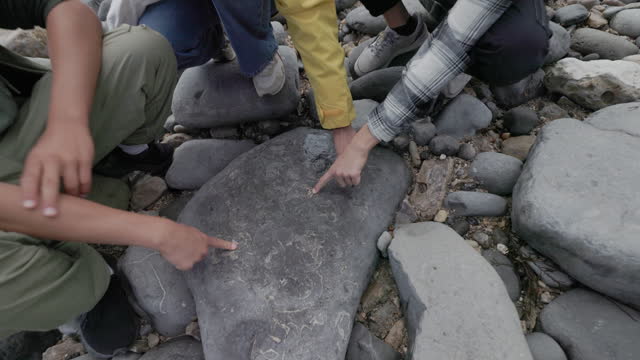 Teenagers examining ammonites in a stone on Lyme Regis Fossil Beach in Dorset, United Kingdom