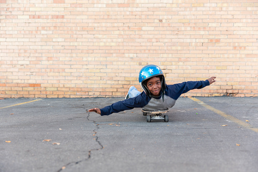 A young boy imagines flying by coasting on a skateboard in the city.  He is ready to take to the skies.