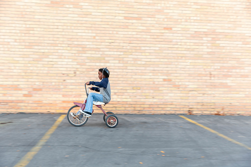 A young boy races on his retro tricycle with visible glee on his face.