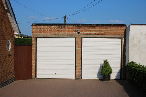 Residential paved driveway with double brick garage, white doors and sky, taken on a clear summers afternoon