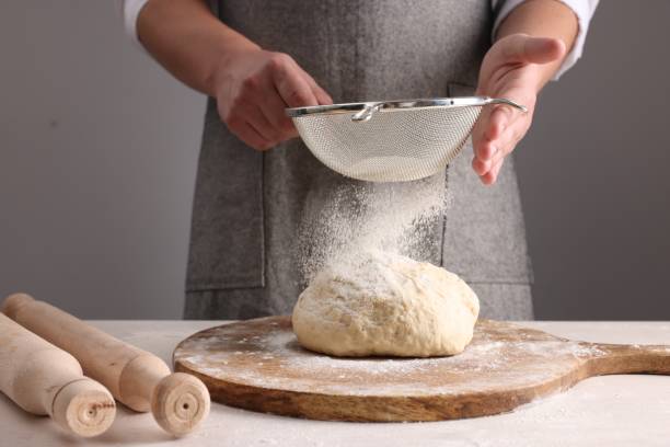 istock Man sprinkling flour over dough at table near grey wall, closeup 1732099111