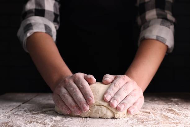 istock Man kneading dough at wooden table on dark background, closeup 1732099119