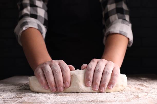 istock Man kneading dough at wooden table on dark background, closeup 1732099687