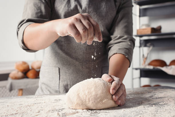 istock Man sprinkling flour over dough at table in kitchen, closeup 1732100224