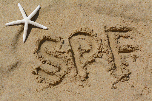 Abbreviation SPF written on sand and starfish at beach, above view