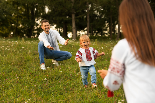 Happy parents in embroidered Ukrainian shirts playing with their cute daughter outdoors
