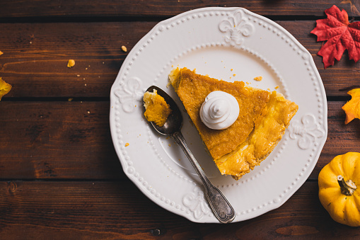 Slice of Thanksgiving holiday pumpkin pie with whipped topping served on a plate