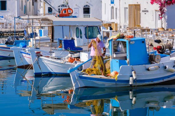 Naousa, GR - 2 August 2023: Fisherman working on a fishing net on his boat