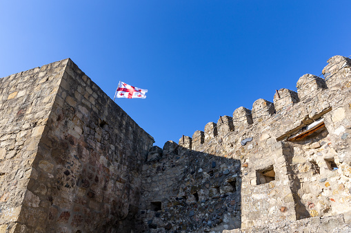 Surami fortress old stone defense crenellated wall with battlements, Georgian national flag on top, Georgia.