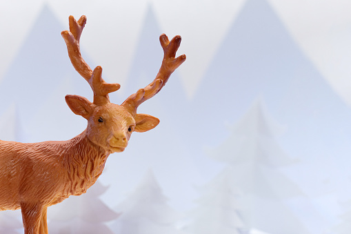 Little reindeer figurine, in the artificial snow, surrounded with pinace an Chrsitmas tree as a Christmas and New year home decoration