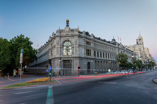 Car lights passing through Alcala street with the facade of the Bank of Spain in the background at dawn in the Spanish capital. Madrid. Spain. July 28, 2023.
