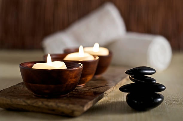Lit candles and black massage stones in Zen spa SEVERAL MORE IN THIS SERIES. Floating aromatherapy candles in wooden bowls and black massage stones rest in a zen spa atmosphere.  Very shallow DOF. hot stone massage stock pictures, royalty-free photos & images