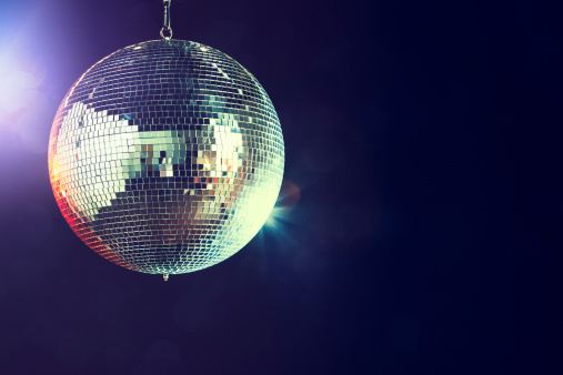 A shining disco ball glitters and spins in a dance club at night, reflecting the various colored lights.  Horizontal with copy space.