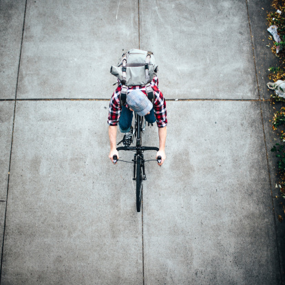 A high angle view of a man commuting in an urban city environment on his street bicycle, a waterproof bike bag on his back.  Square crop with copy space.