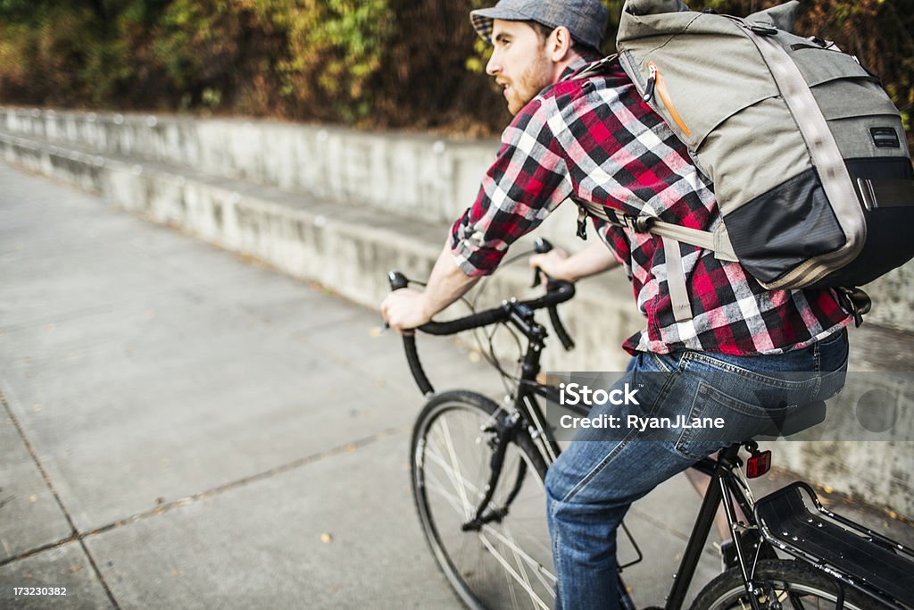 Bike Commuter in Portland Oregon A young man commuting in an urban city environment on his street bicycle, a waterproof bike bag on his back.  This is the Eastbank Esplanade in Portland, Oregon, that follows along the Willamette river.  Horizontal with copy space. Bicycle Stock Photo