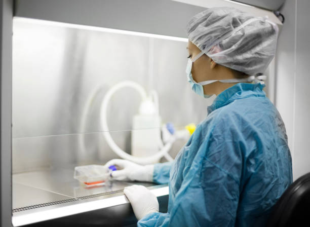 Woman working in a Cell culture hood Woman working with a cell cutture flask. She is doing cancer research. pharmaceutical manufacturing machine stock pictures, royalty-free photos & images