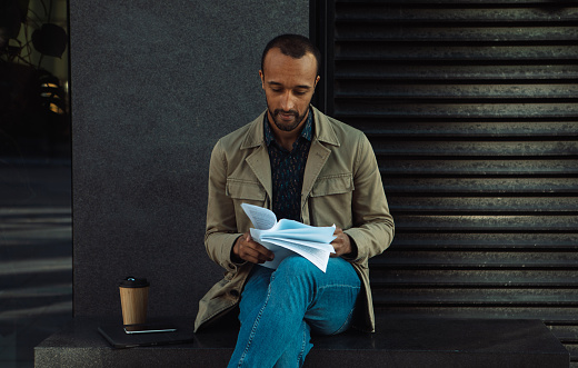A young black man looks through documents while sitting at a bus stop. Lifestyle concept,