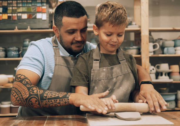 Pottering with son. Confident young man and little boy making ceramic pot on the pottery class