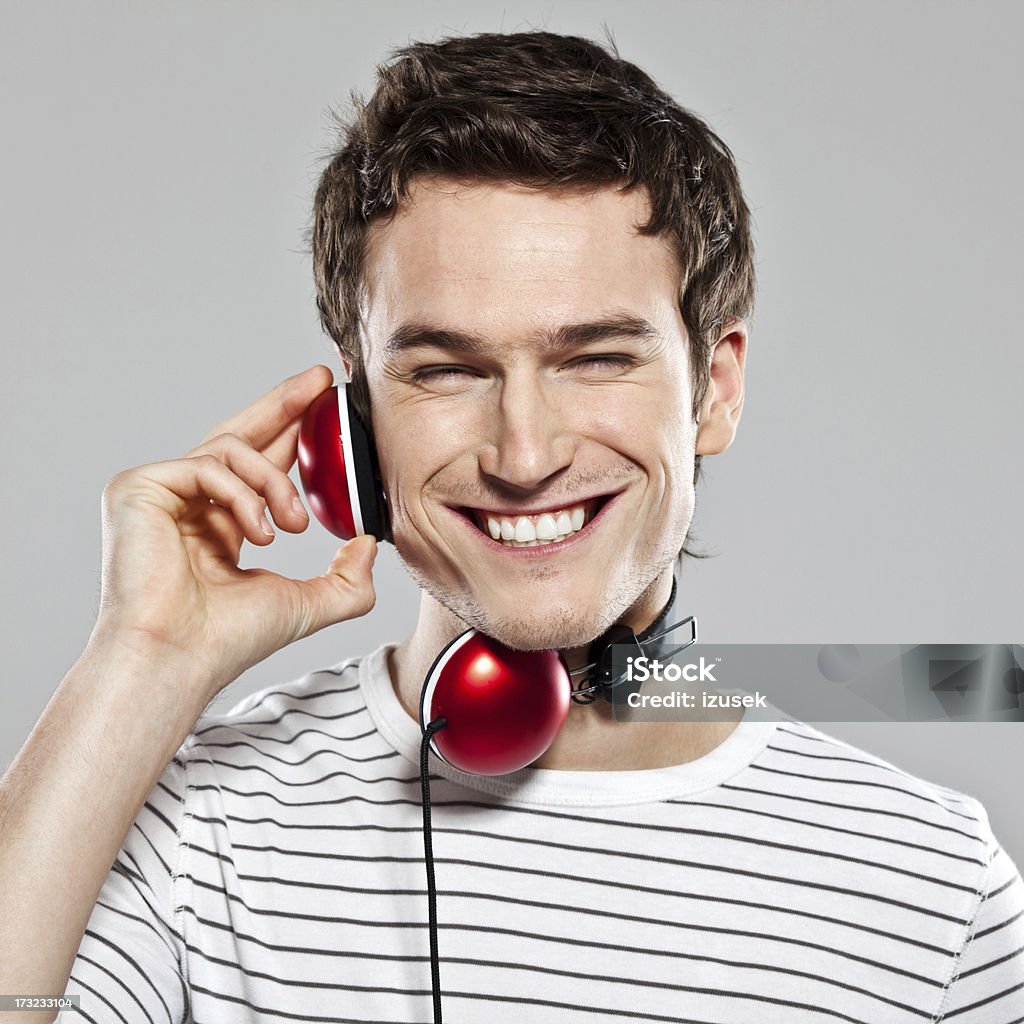 Young man listening to music Portrait of happy young man wearing headphone and listening to the music, laughing at camera. Studio shot, grey background. 20-24 Years Stock Photo
