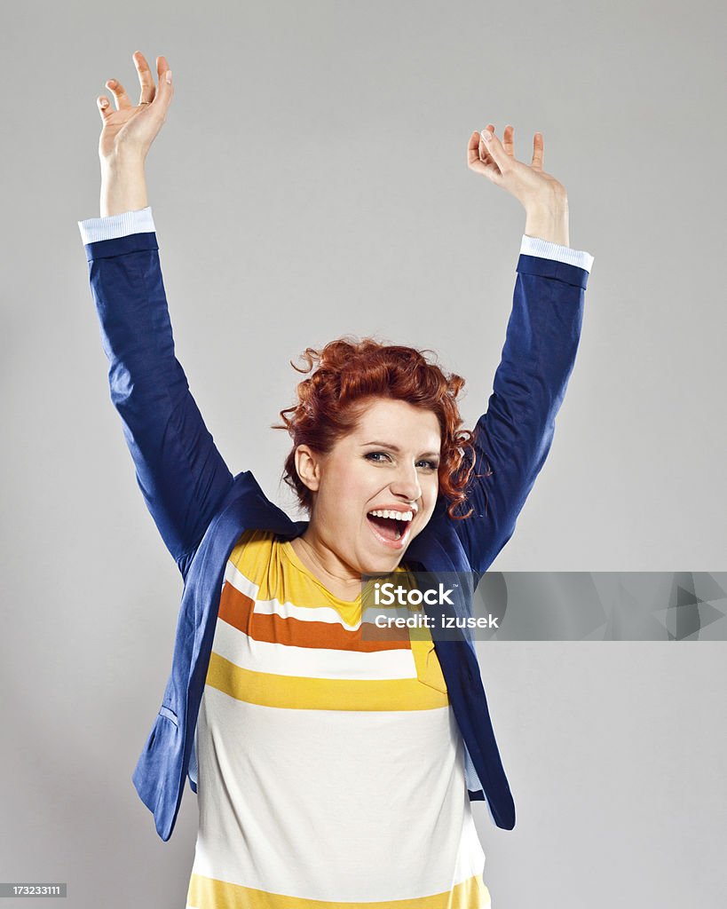 Success Portrait of happy young woman, raising her arms and laughing at camera. Studio shot, grey background. 25-29 Years Stock Photo