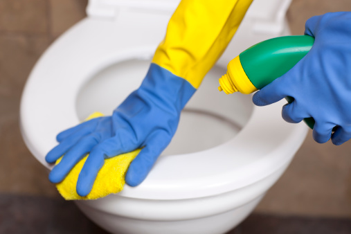 Unrecognized person cleaning the toilet with a yellow rag wearing gloves.