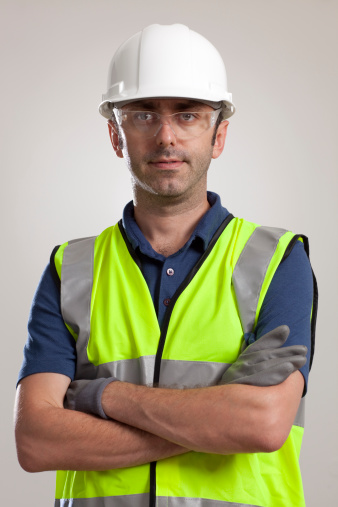 portrait of a manual worker in protective gear (helmet, gloves, reflective clothing) wearing goggles.