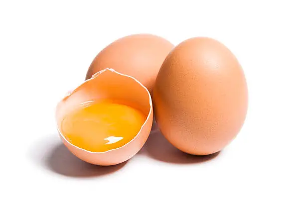Group of brown raw chicken eggs, one is broken, yolk egg visible, isolated on white, studio shot.