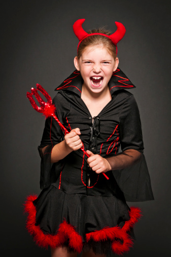 Portrait of 9 years old girl in a devil costume is laughing and screaming, isolated on black, studio shot.
