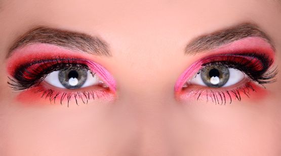macro shoot of woman green eyes with pink and orange makeup.