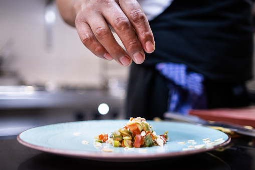 A hand finishing plating the food on the dish inside the restaurant kitchen