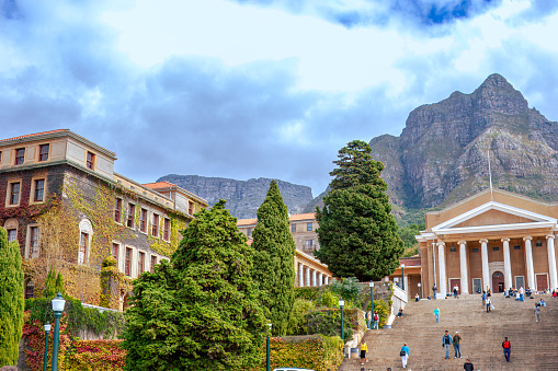 The University of Cape Town in South Africa. Photo shot in the afternoon sunlight; vertical format. Some cars are parked in front of the steps to the building. Many students can be seen walking away or to the building; some just sit on the steps relaxing or chatting with friends. Note to inspector: Several people can be seen in the image but none is more prominent than the other which I understand is acceptable to iStock for Creative images.