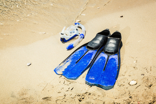 Scuba diving mask and fins on sandy beach.
