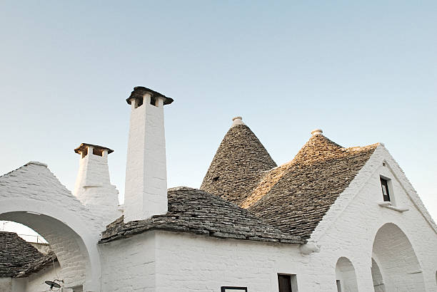 I tetti dei trulli di Alberobello sono a cono, composti da un doppio strato di pietre: un rivestimento interno a volta e un cono esterno impermeabile di chiancarelle (lastre di pietra calcarea). Sono coronati da pinnacoli, elementi decorativi che spesso recano le iniziali del costruttore, e da simboli bianchi a calce (religiosi, apotropaici o astrologici), che rappresentano un tratto distintivo e misterioso di queste costruzioni uniche