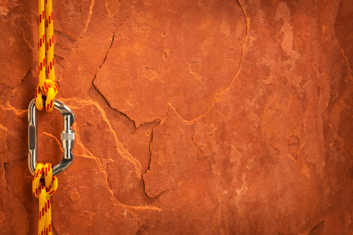 This is a photo taken in the studio of yellow climbing rope attached to a carabiner with a clove hitch knot on each end in front of a sheet of red rock.