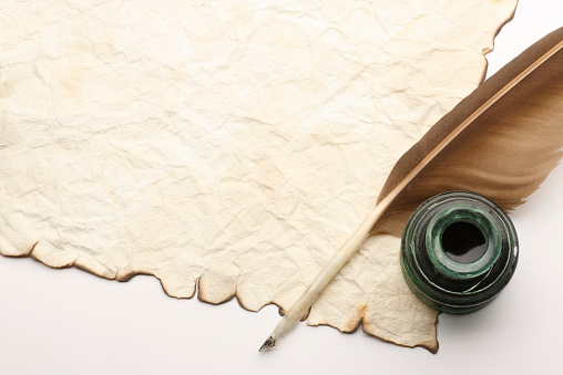 A quill and inkwell sitting on an old blank document.