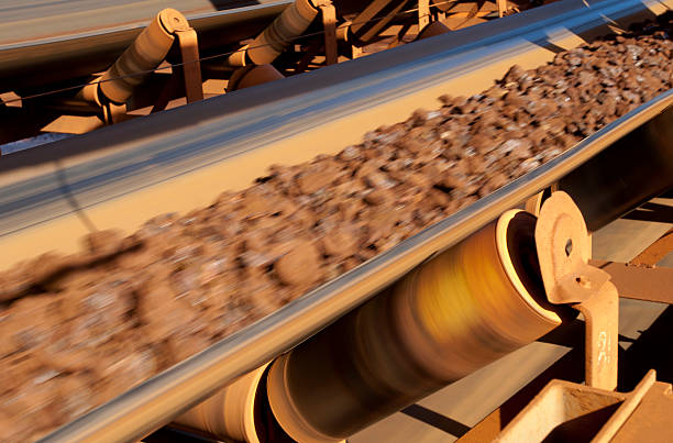 Conveyor belt carrying ore at a minesite. A conveyor belt rapidly carrying crushed ore on a mine site. mining conveyor belt stock pictures, royalty-free photos & images